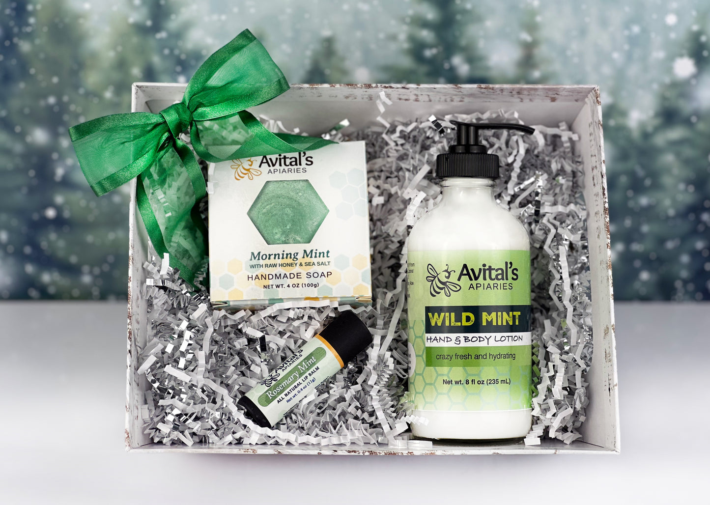A gift set containing Avital's beeswax and shea butter lip balm, wild mint lotion, and rosemary mint salt soap, all displayed in a festive market basket with green decor.