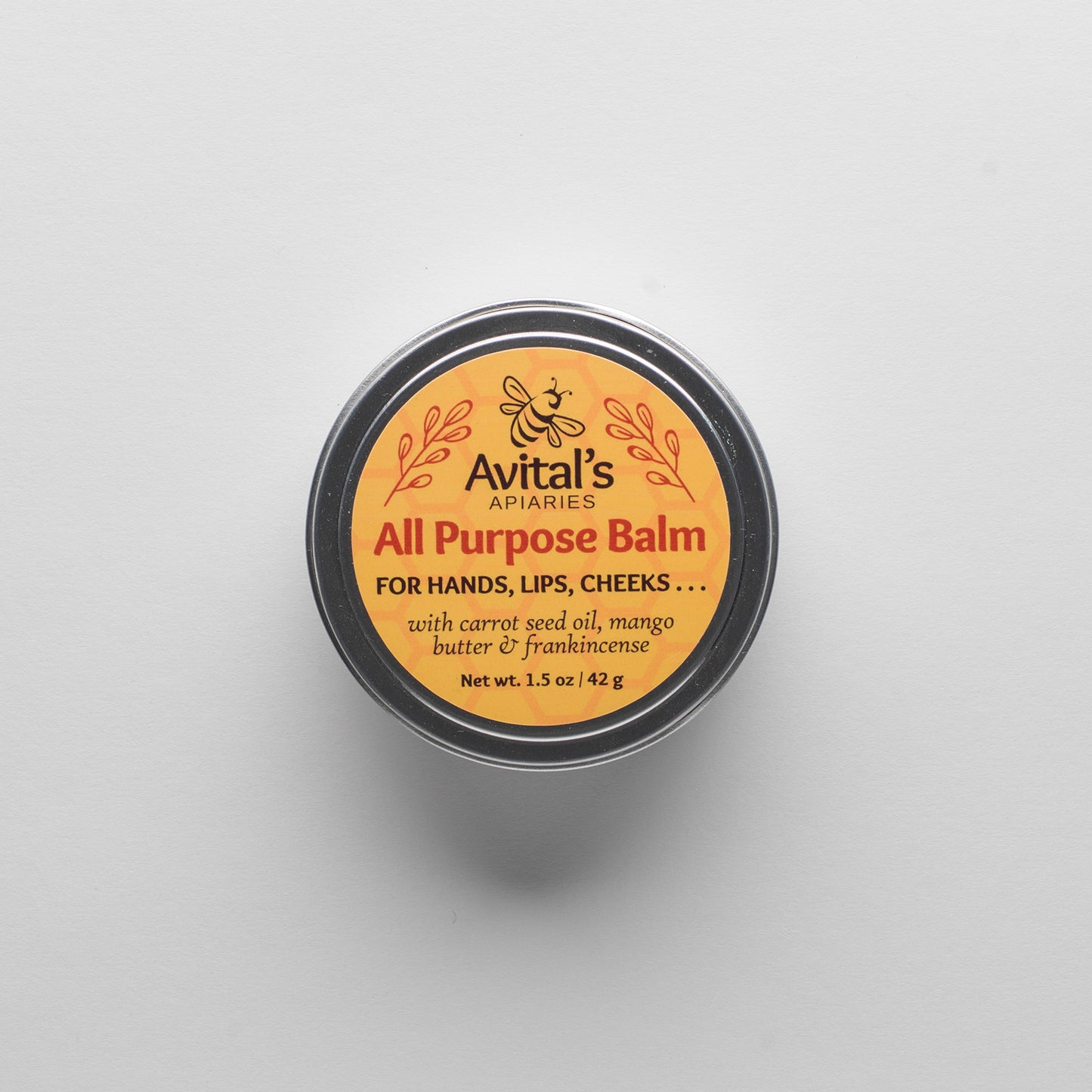 An overhead shot of a tin of All purpose balm. The label is golden yellow with red text: All Purpose Balm for hands, lips, cheeks... with carrot seed oil, mango butter & frankincense
