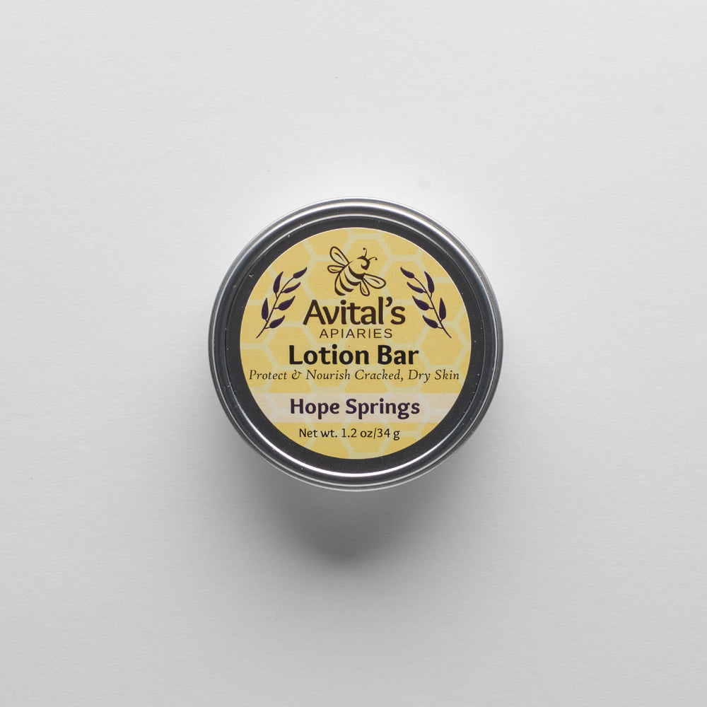 
                  
                    Overhead shot of a tin containing a Hope Springs Lotion bar. The label is a cheerful yellow  with a hexagon pattern and says "Lotion Bar. Proptect & Nourish Cracked, Dry Skin. Hope Springs. 1.2 oz
                  
                