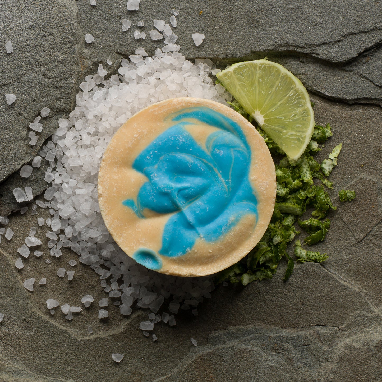 A round, gold and blue bar of soap surrounded by citrus peel and salt