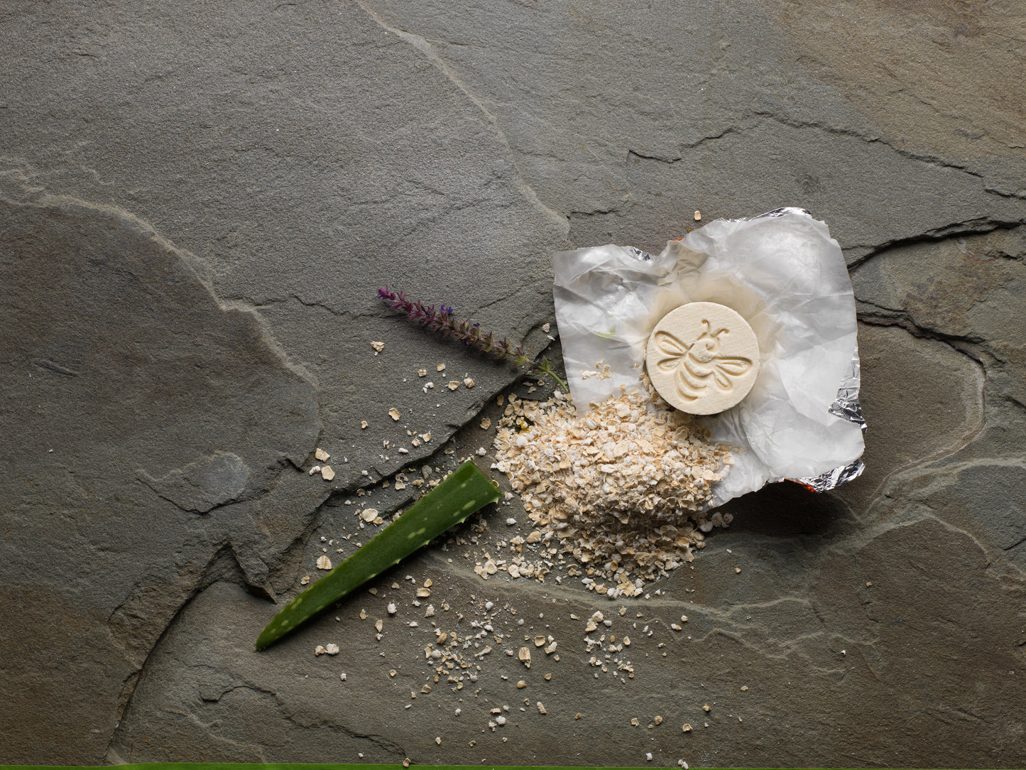 A bath fizzy with a small pile of oats, an aloe leaf, and a sprig of lavender.