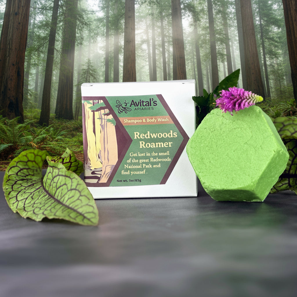 A green bar of shampoo and body wash with a floral design, placed next to a white box with the label 'Redwoods Roamer'. There are leaves and a flower decoration around the products, and Redwoods National Park in the background.