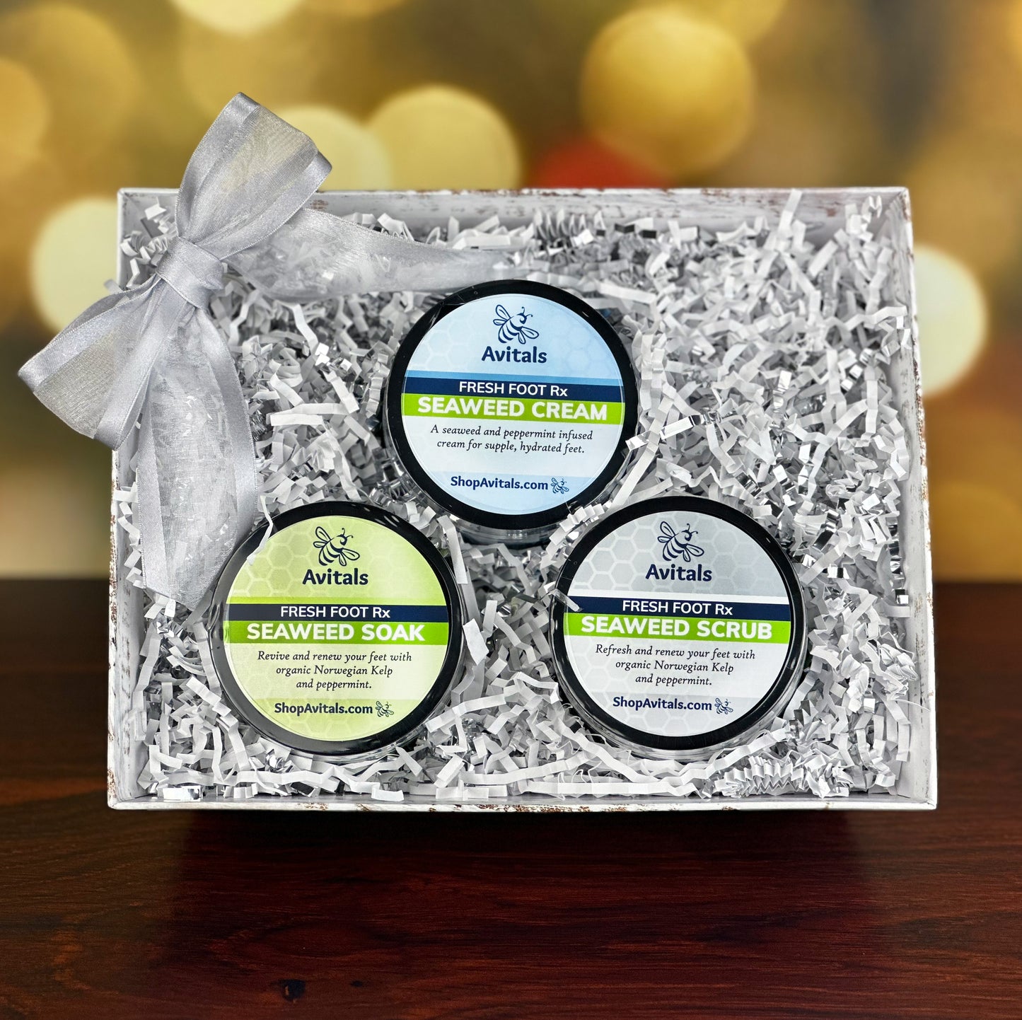 A gift set containing three jars of Avital's seaweed and peppermint foot care products, including a soak, scrub, and cream, presented in a decorative market tray with a bow.