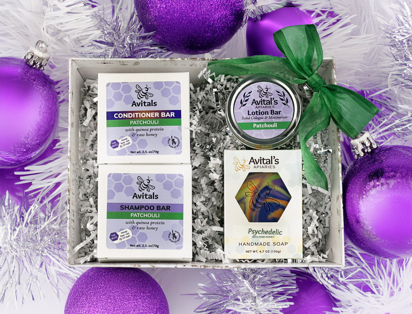 A gift set containing patchouli-scented products —shampoo bar, conditioner bar, soap bar, and lotion bar —packaged in a box with purple decorations and a green bow.