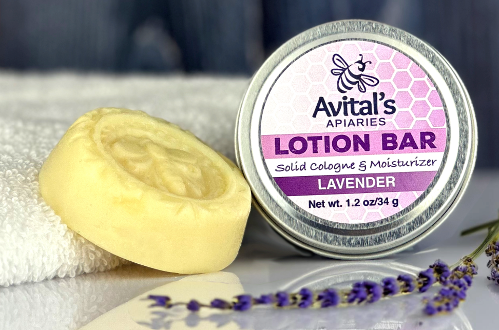 A lotion bar and its packaging with 'Avital's Apiaries' branding, alongside a sprig of lavender.