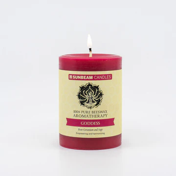 A reddish-pink lit pillar candle with a paper label.