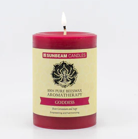 A reddish-pink lit pillar candle with a paper label.