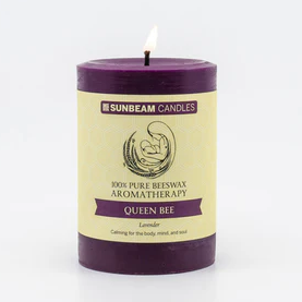 A lit deep purple pillar candle with a paper label.