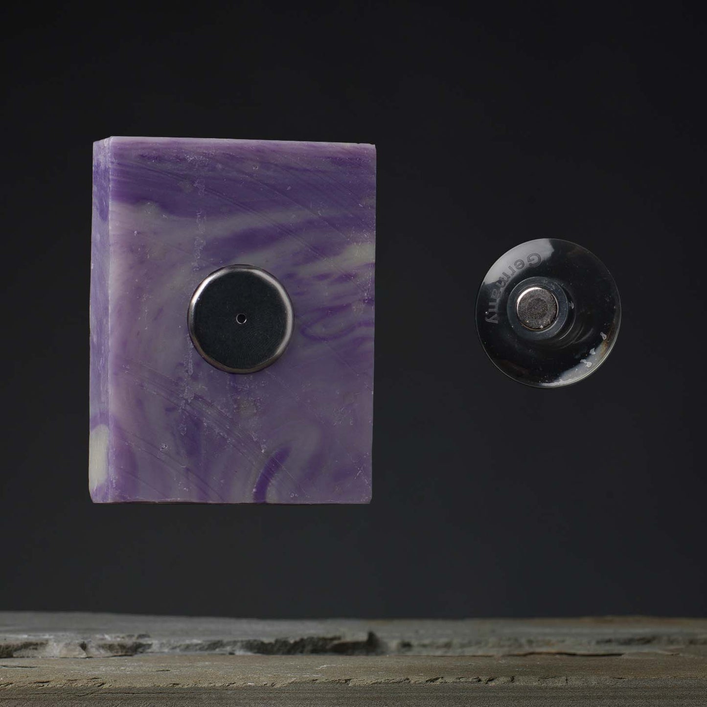 A purple soap bar attached to a suction cup mounted on a dark wall.
