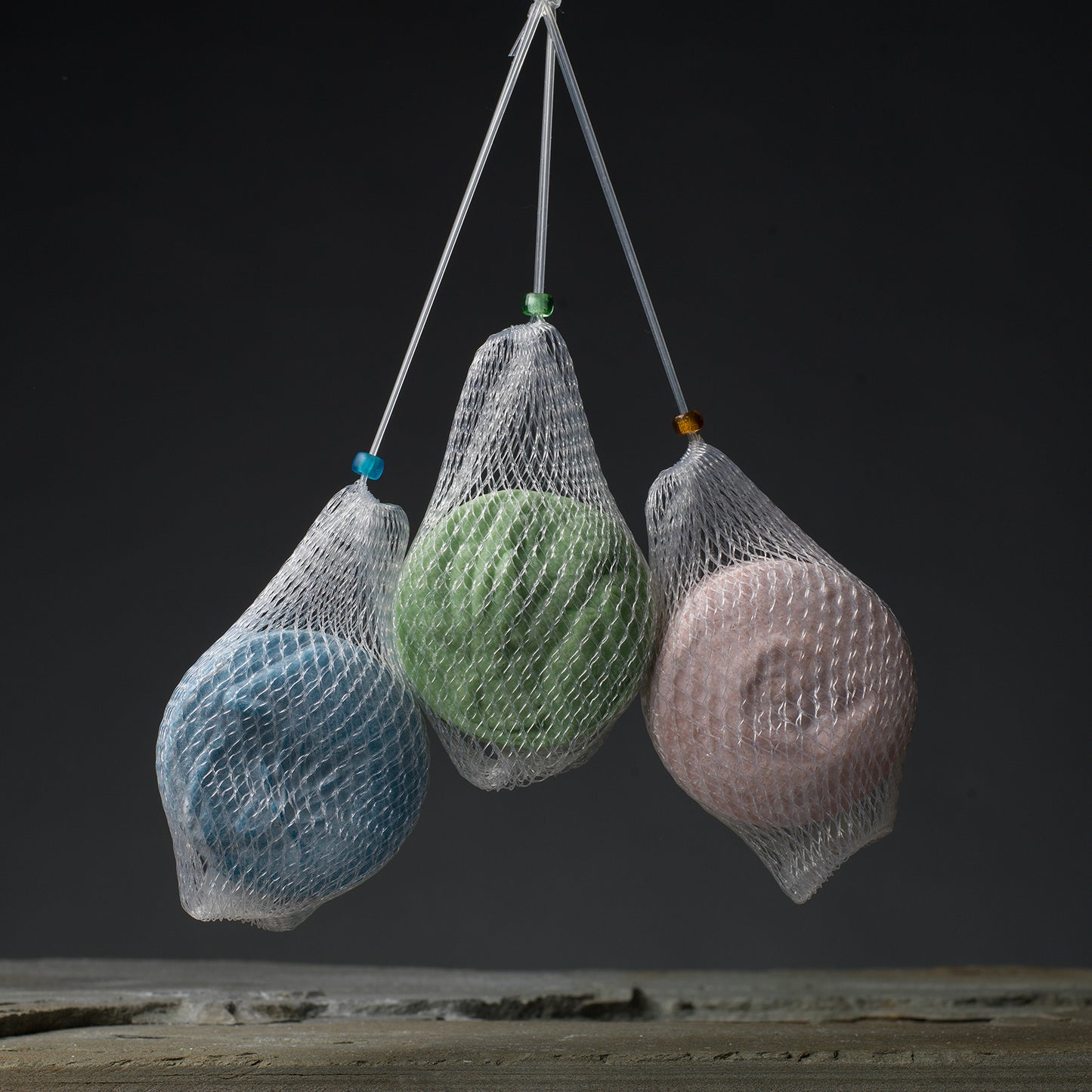 Three soap nets holding colorful round soups suspended over a granite ledge.