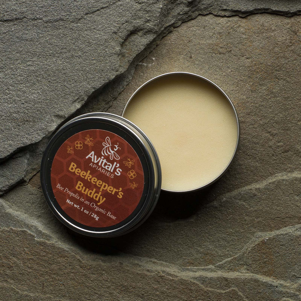 A tin of Beekeeper's Buddy open to see the creamy balm inside. The label is reddish brown with gold accents and says: Bee Propolis in an organic base
