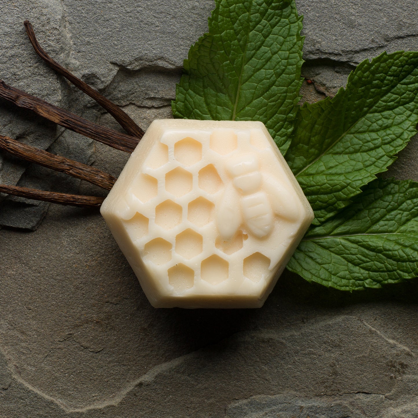 A conditioner bar with a honeycomb pattern texture, presented next to vanilla and mint leaves.