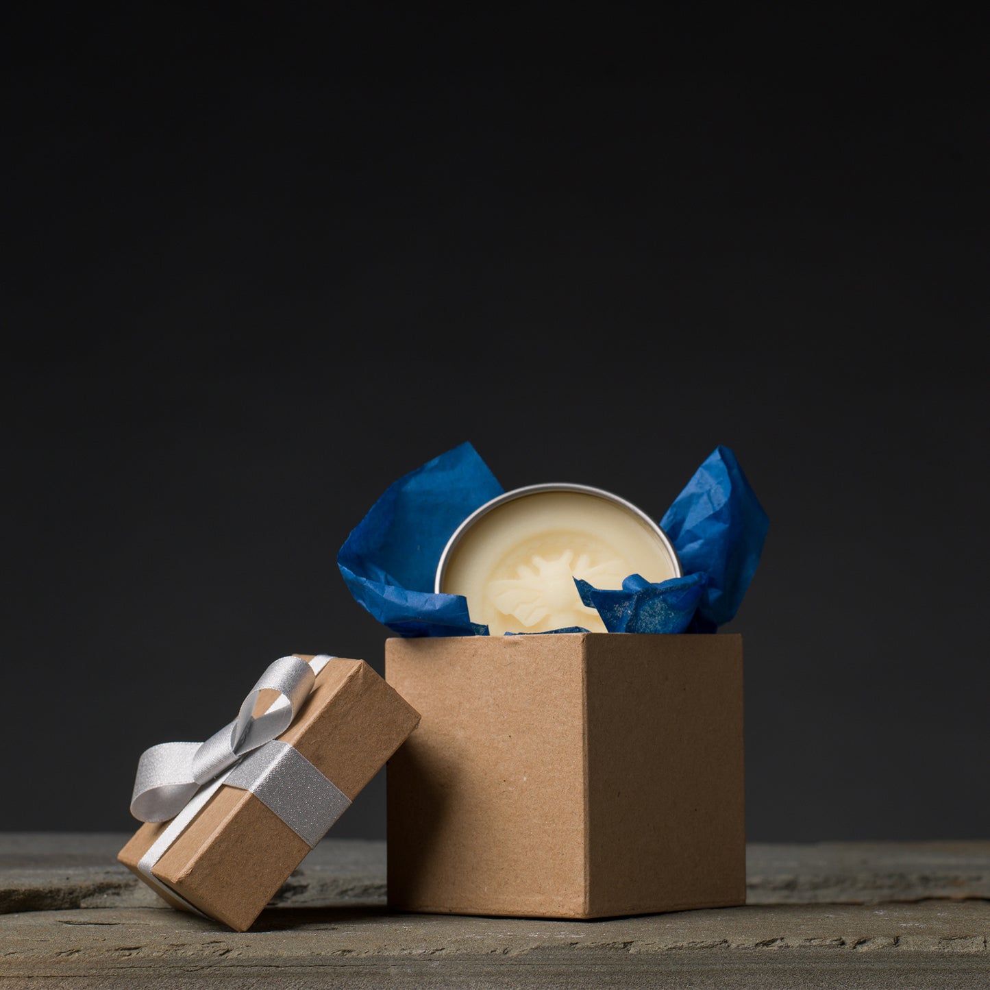A kraft box with silver bow. Dark blue tissue peeks out along with a honey bee stamped lotion bar.